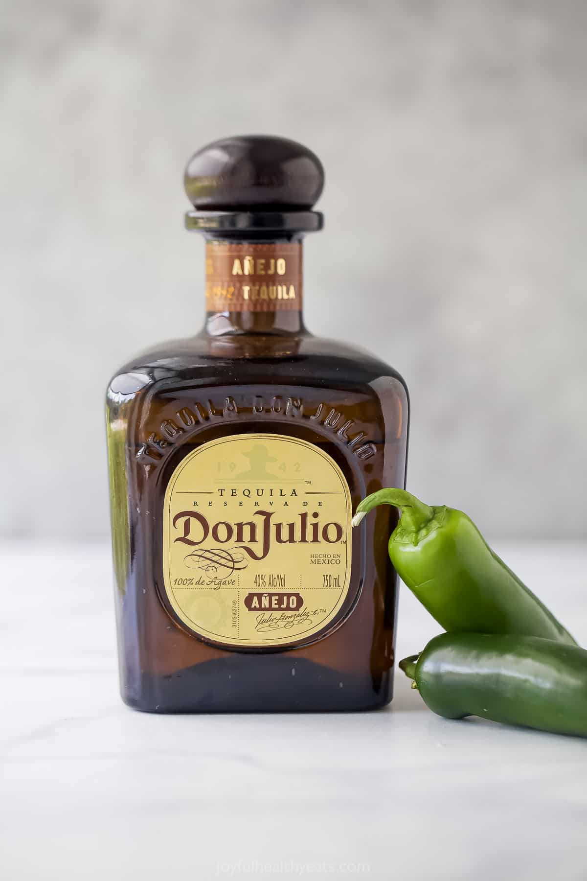 A bottle of Don Julio tequila on a kitchen countertop beside two fresh jalapeños