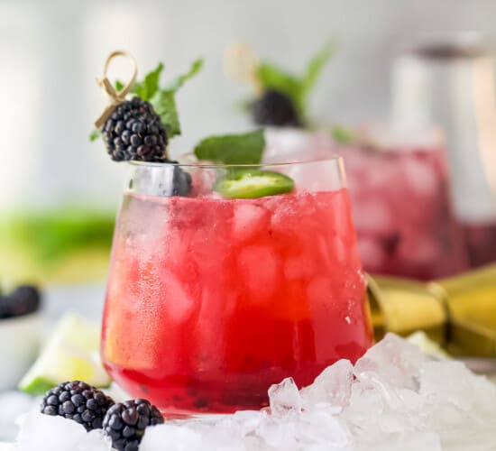 A spicy blackberry margarita in a glass with a second marg and a jar of homemade simple syrup in the background