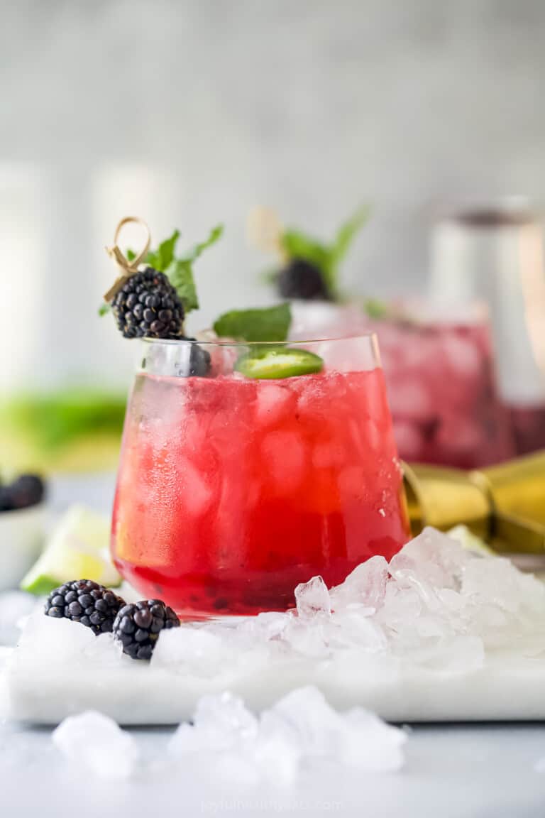 A spicy blackberry margarita in a glass with a second marg and a jar of homemade simple syrup in the background