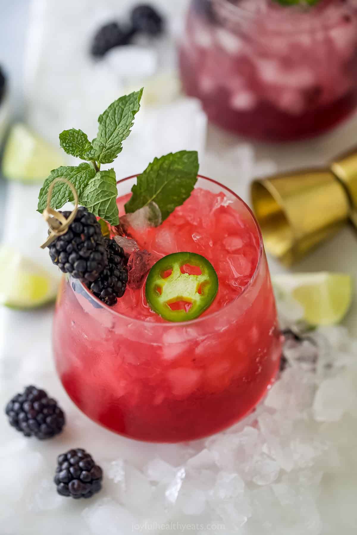 A spicy blackberry margarita in a short cocktail glass with fresh fruit surrounding it