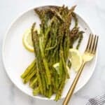 A plate full of roasted asparagus with three lemon slices and a fork beside the veggies