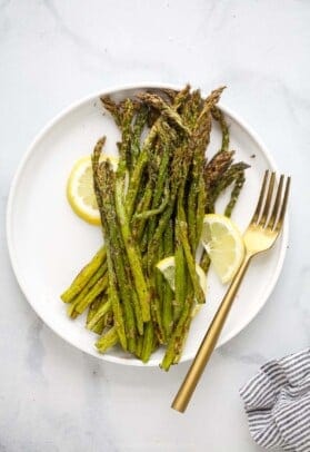 A plate full of roasted asparagus with three lemon slices and a fork beside the veggies