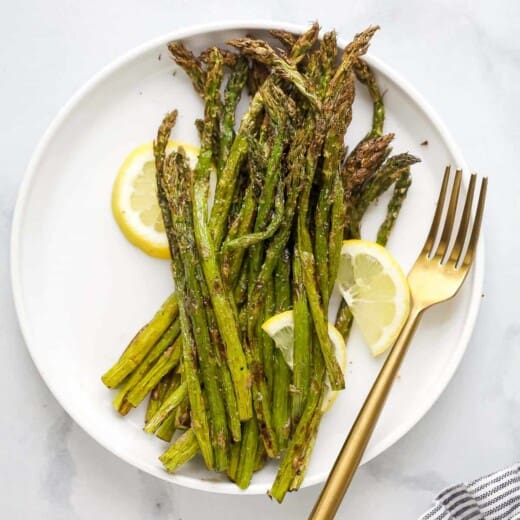 A plate full of roasted asparagus with three lemon slices and a fork beside the veggies