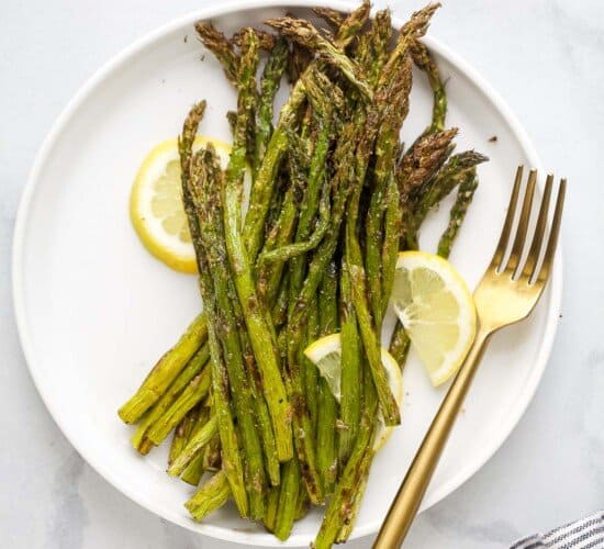 A plate full of roasted asparagus with three lemon slices and a fork beside the veggies