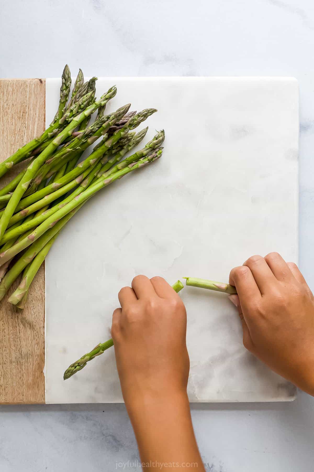 A pair of hands snapping the tough end off of an asparagus stalk