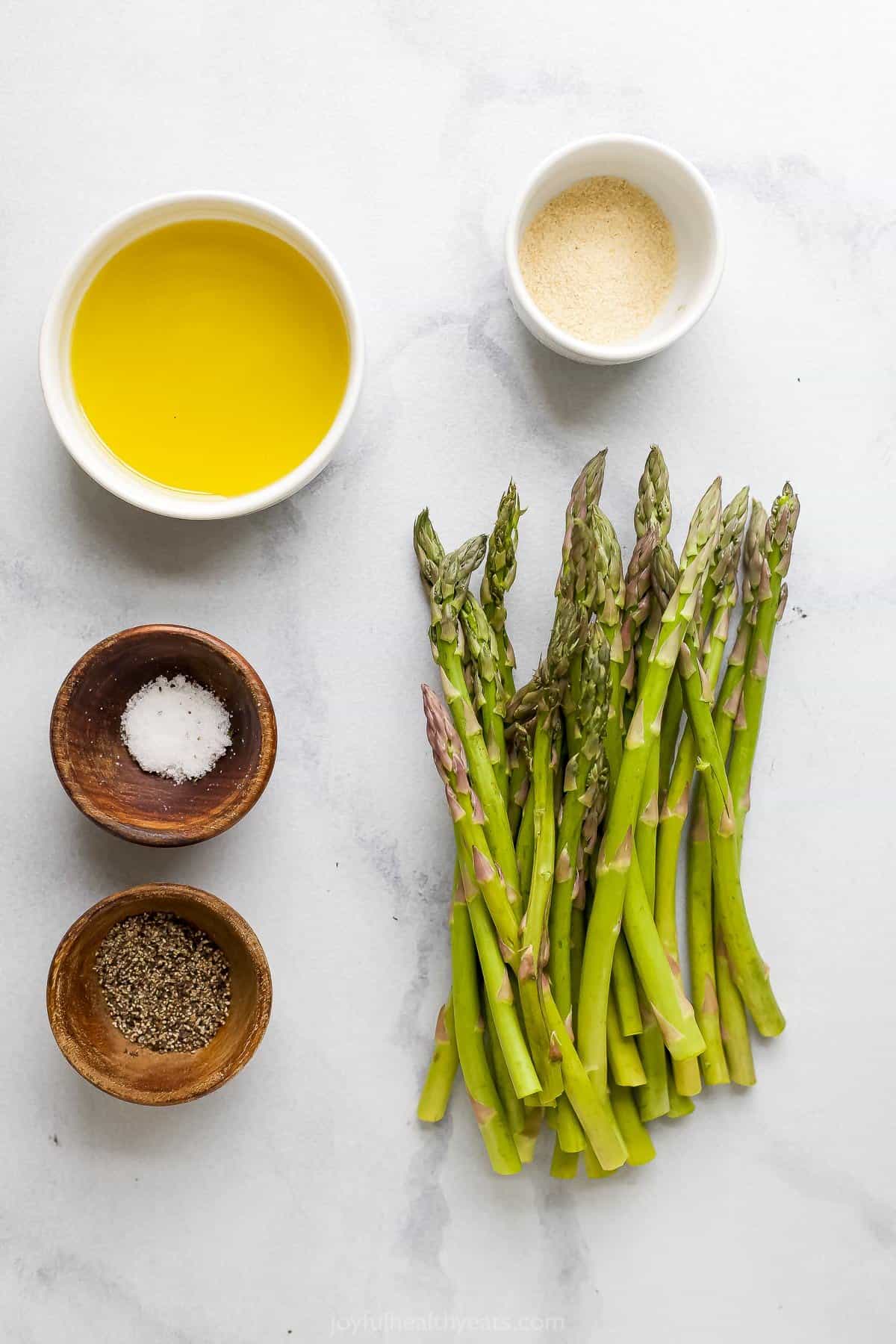 Trimmed asparagus, salt, pepper and oil arranged neatly on a kitchen countertop