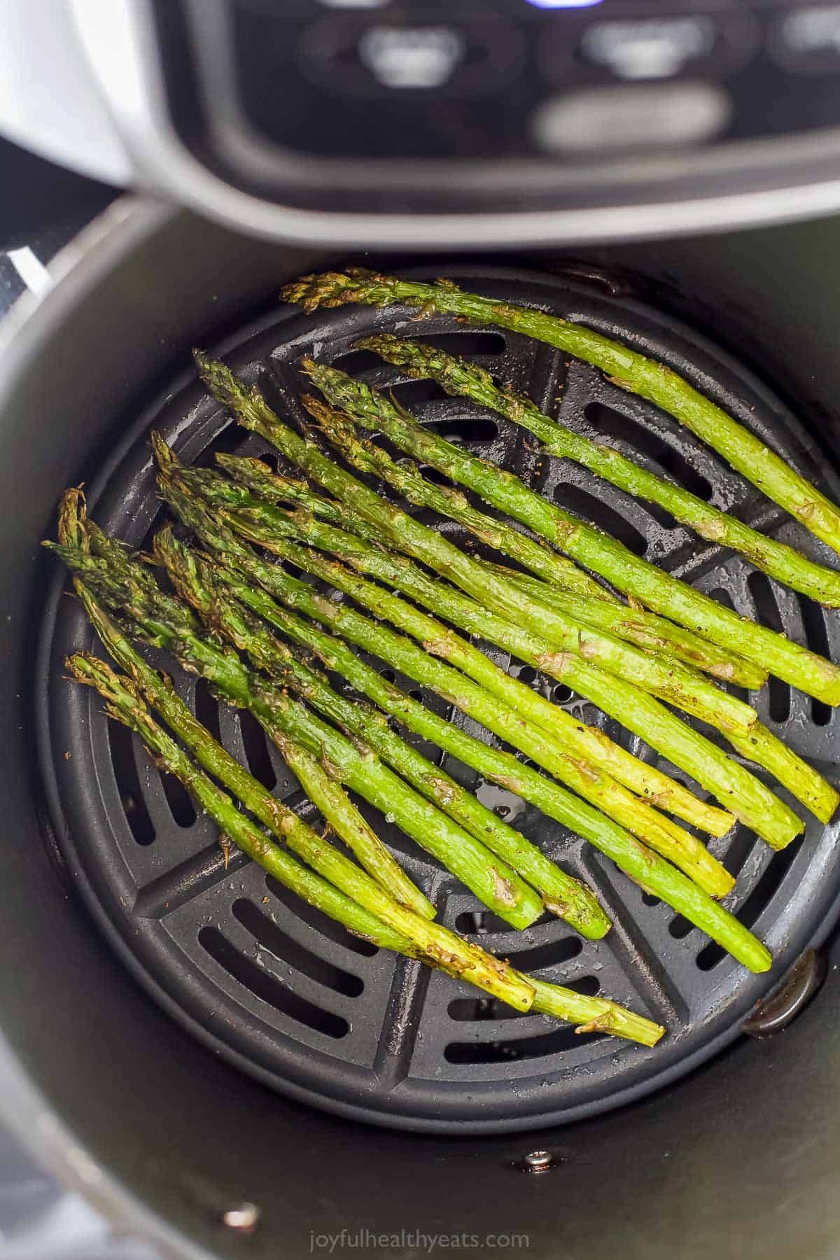 One batch of seasoned asparagus inside of an Air Fryer basket