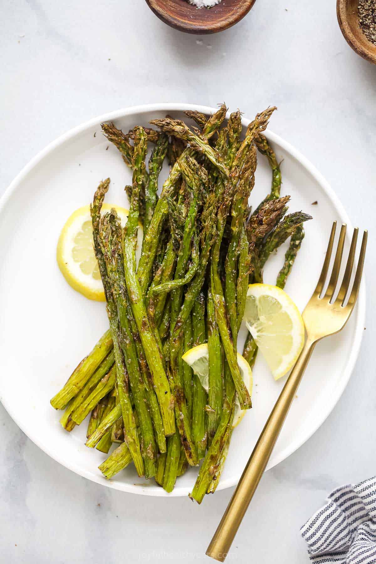Air Fryer asparagus stalks on a plate with a raised rim on top of a marble counter