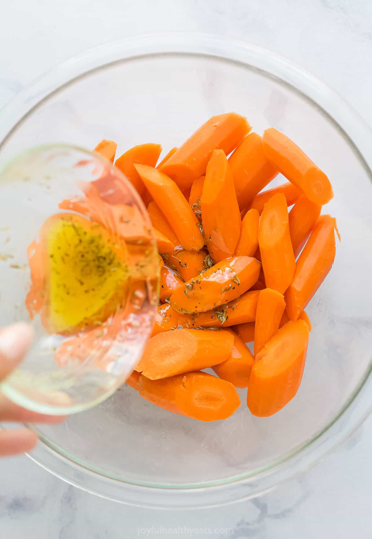 pouring seasoned olive oil over a bowl of cut up carrots