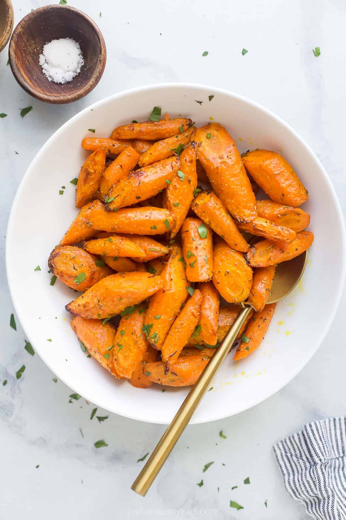 roasted and seasoned carrots in a white bowl with a gold spoon