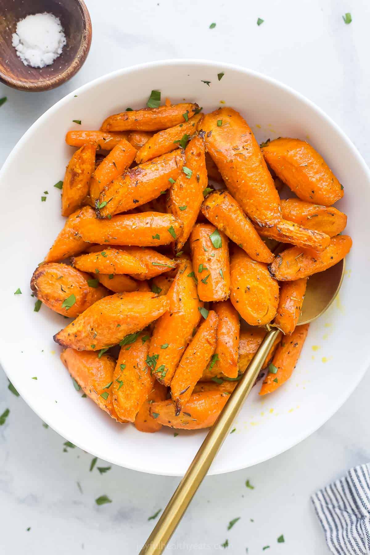 roasted and seasoned carrots in a white bowl with a gold spoon