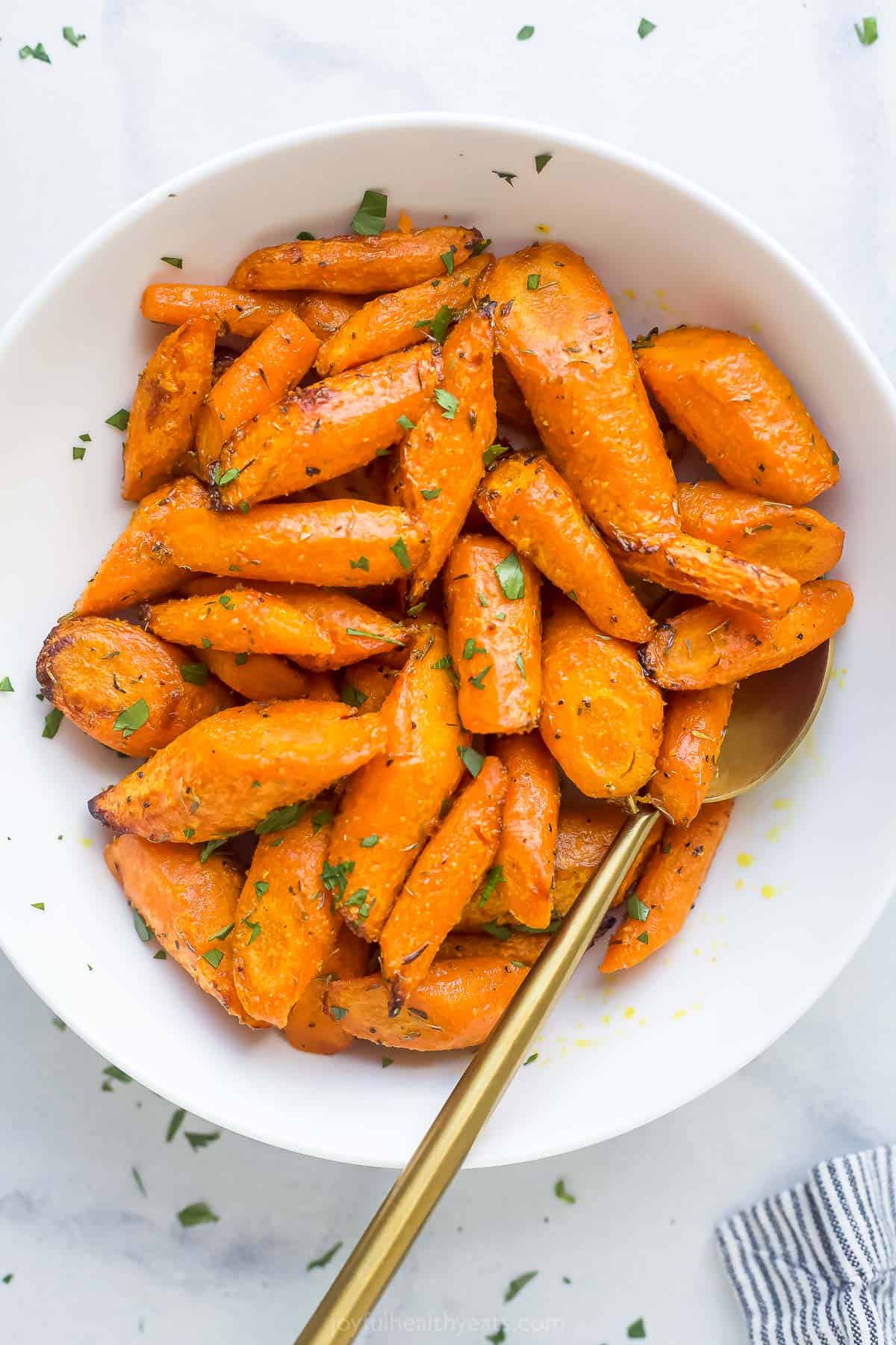 roasted and seasoned carrots in a white bowl with a gold spoon