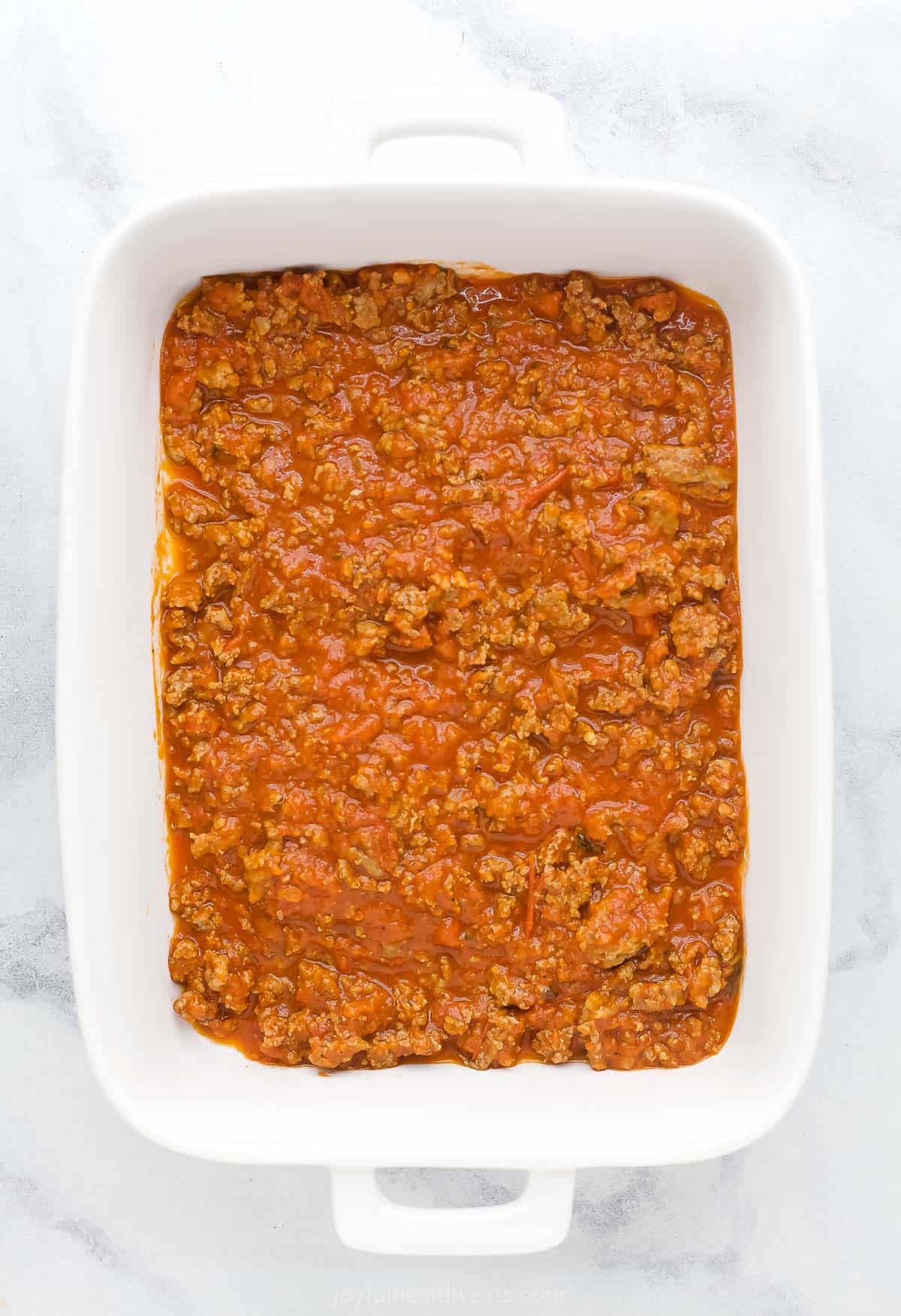 A baking dish with a layer of homemade meat sauce on the bottom
