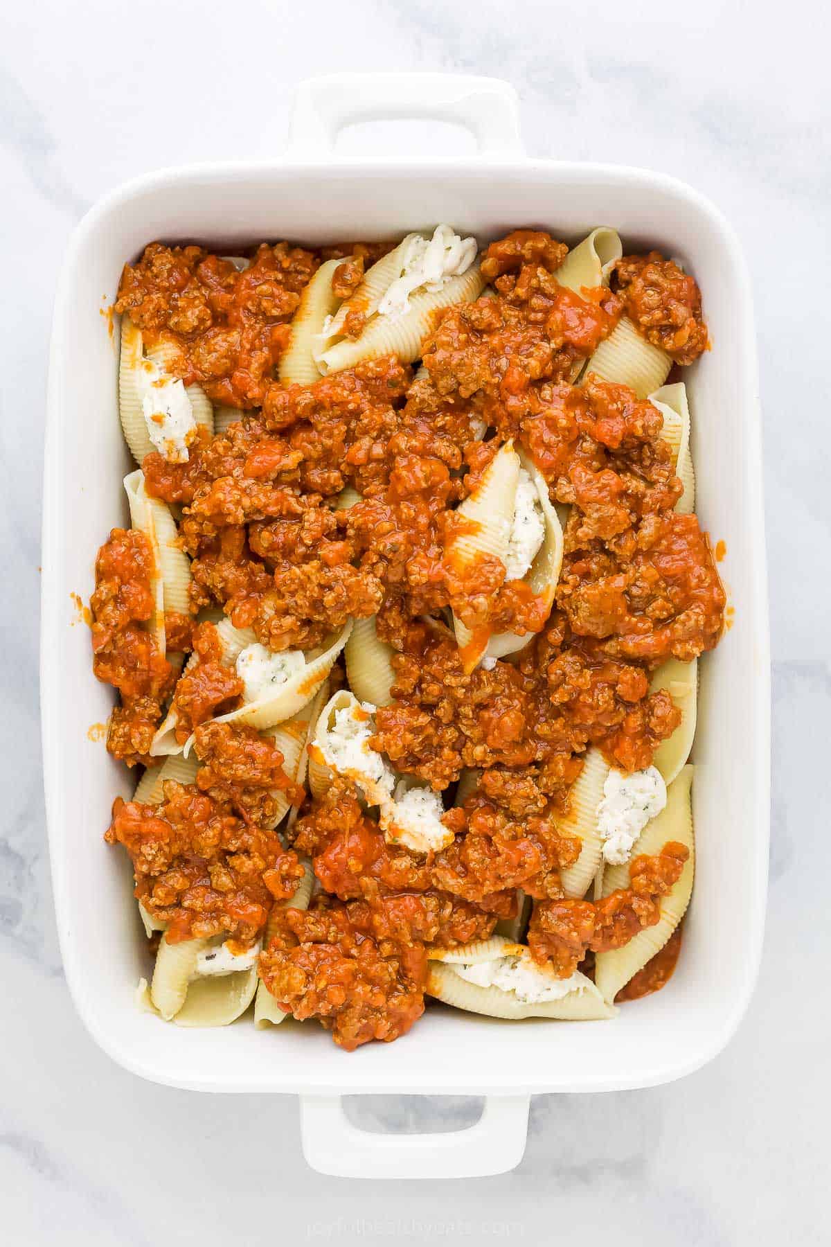 A layer of stuffed shells sandwiched between two layers of homemade Ragu in a casserole dish