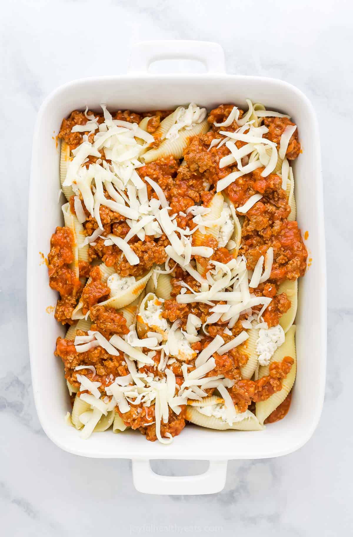The unbaked stuffed shells and meat sauce in a casserole dish after the mozzarella has been added