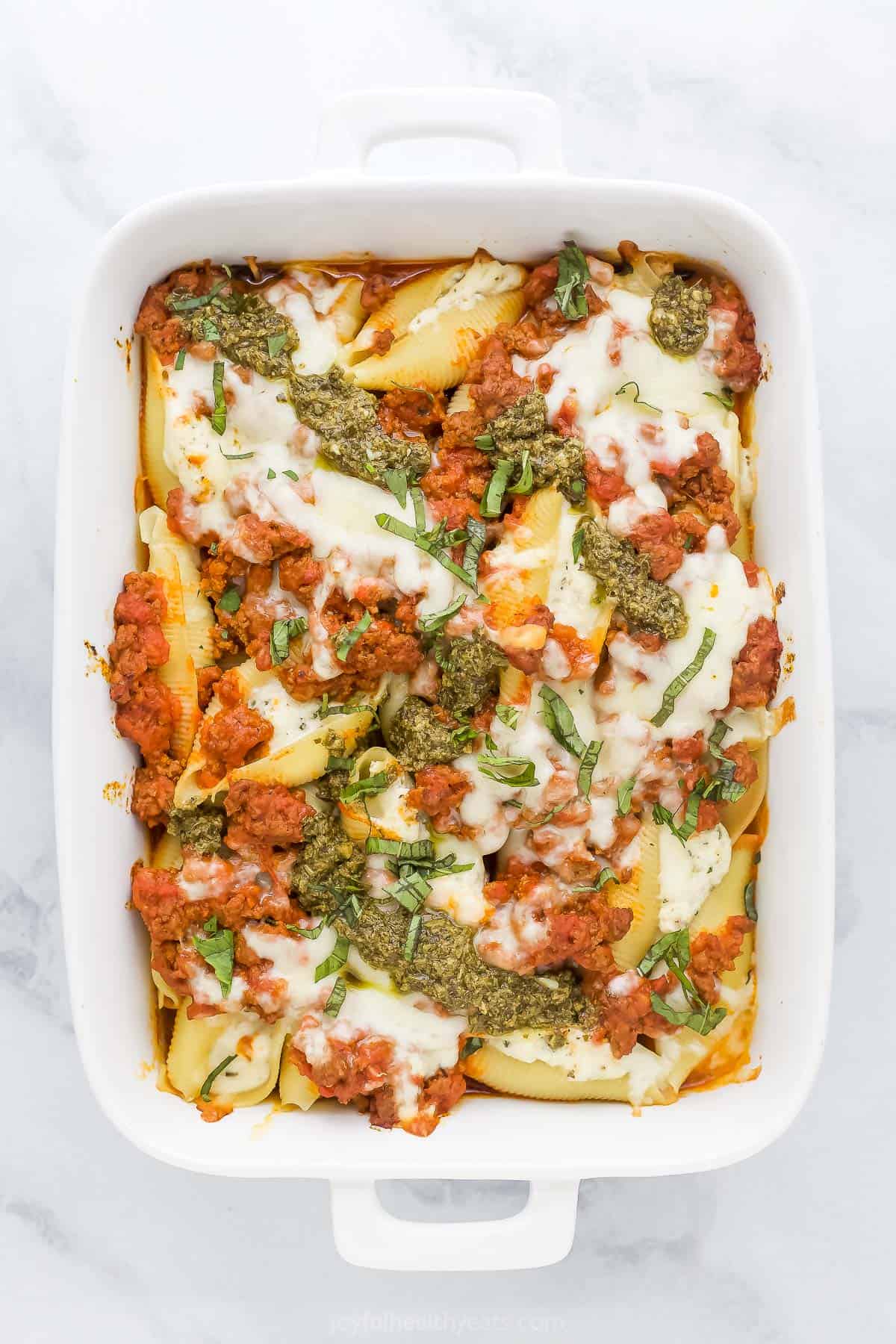 Baked stuffed shells with meat inside of a casserole dish with pesto sauce and mozzarella cheese on top