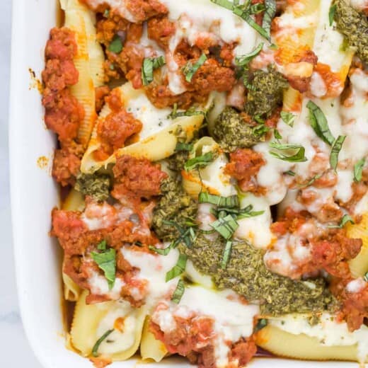 A white baking dish containing cheese stuffed shells with meat sauce and a drizzle of pesto