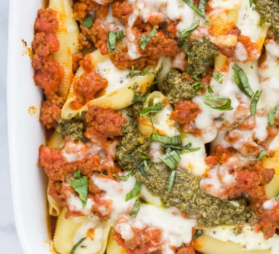 A white baking dish containing cheese stuffed shells with meat sauce and a drizzle of pesto