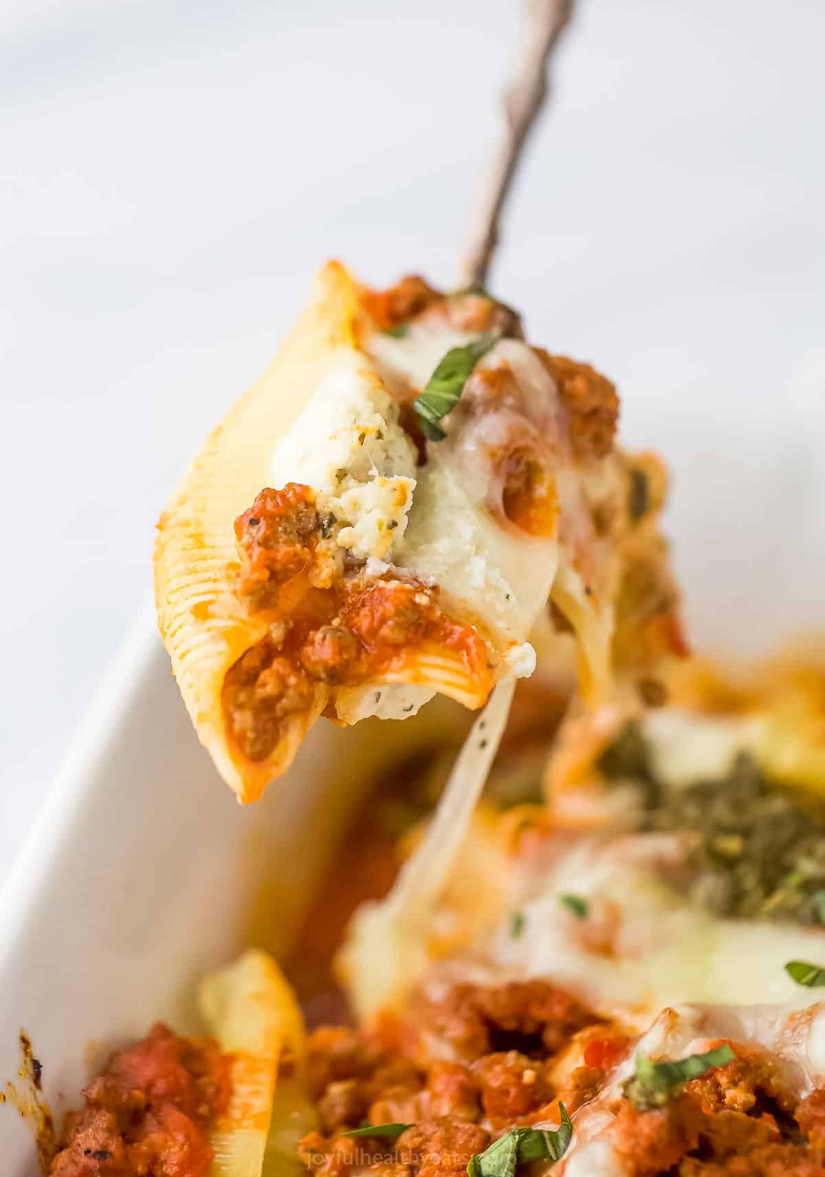 A spoon lifting a ricotta stuffed shell from a baking dish full of stuffed shells