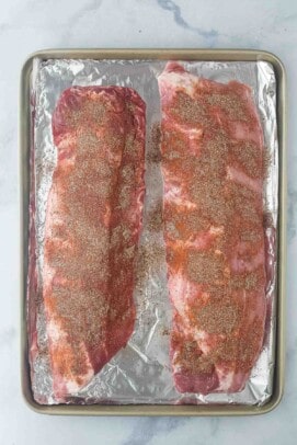 two seasoned racks of ribs on a foil lined sheet tray