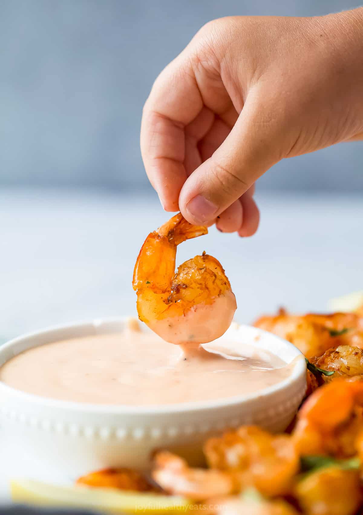 someone dipping shrimp into a pale red dipping sauce