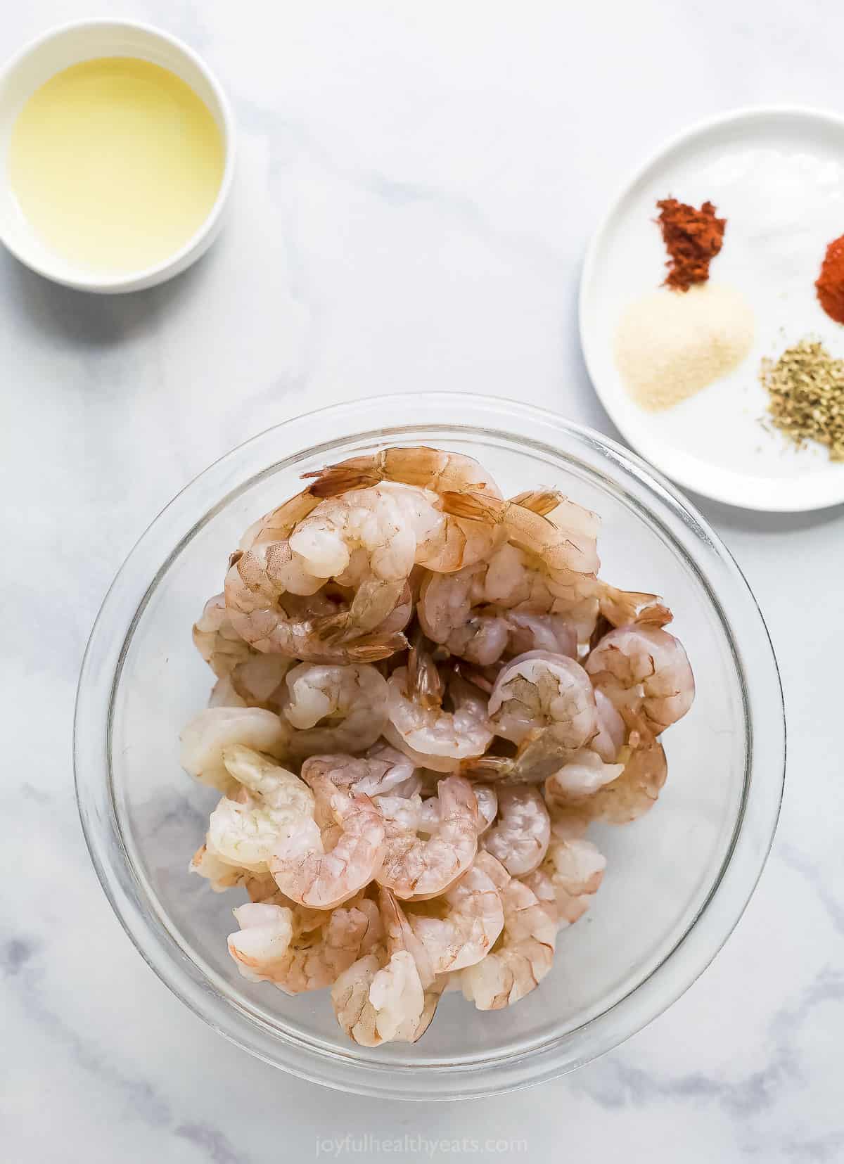 a bowl of raw shrimp, a plate with dried seasonings, and small bowl with cooking oil