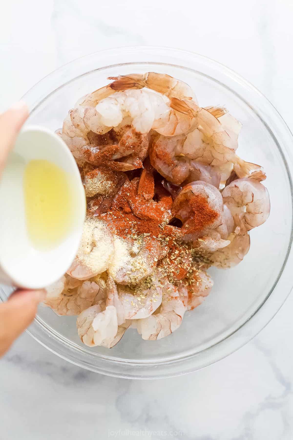 a bowl of raw shrimp being seasoned with spices and oil