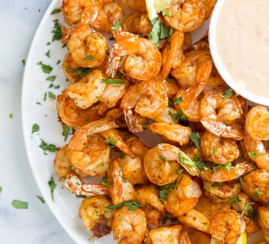 a plate of cooked shrimp with a side of dipping sauce