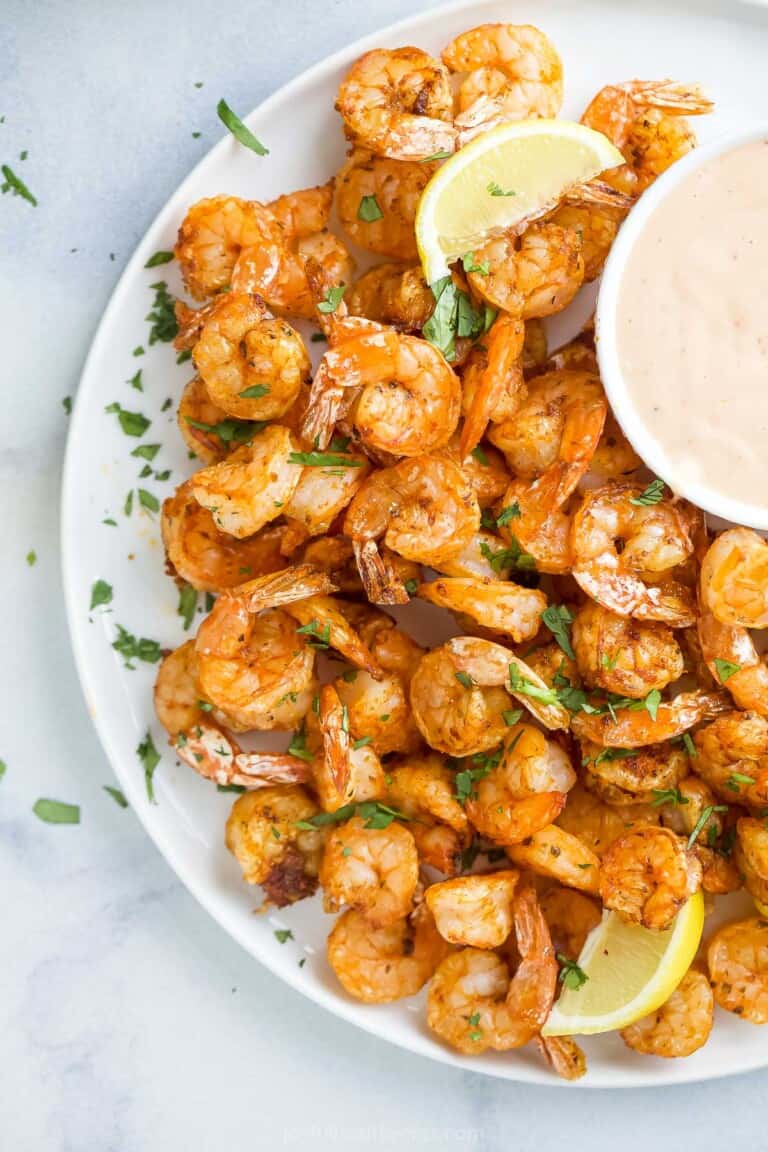 a plate of cooked shrimp with a side of dipping sauce