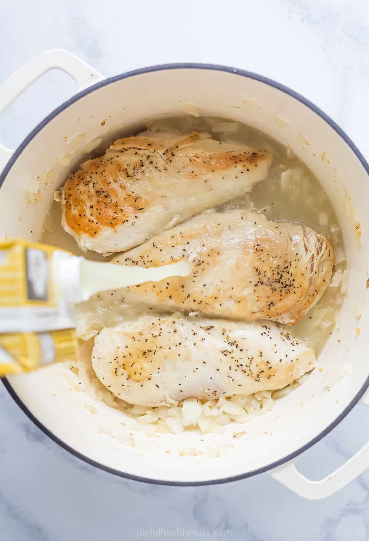 pouring chicken stock over seared chicken breasts in a pot