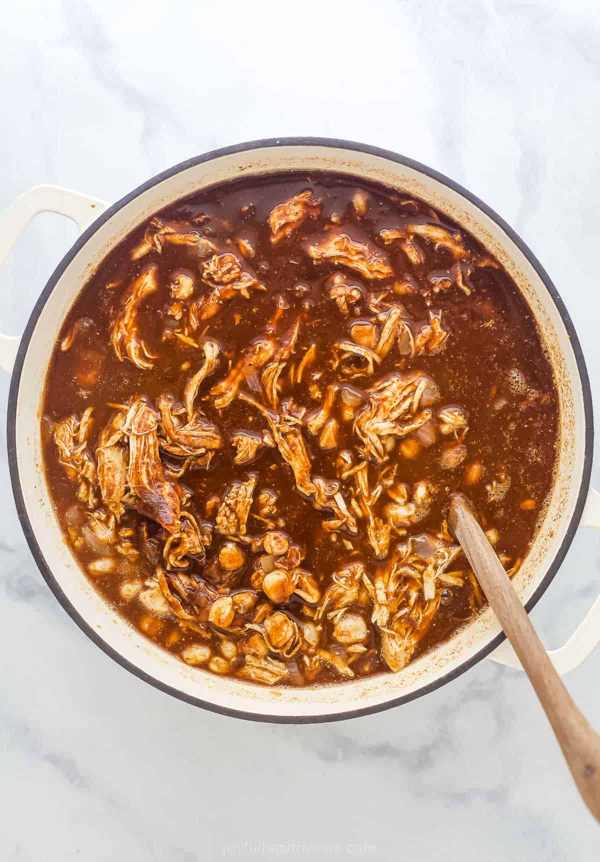 a pot of Mexican Chicken Stew with bits of pulled chicken and hominy in a brown broth