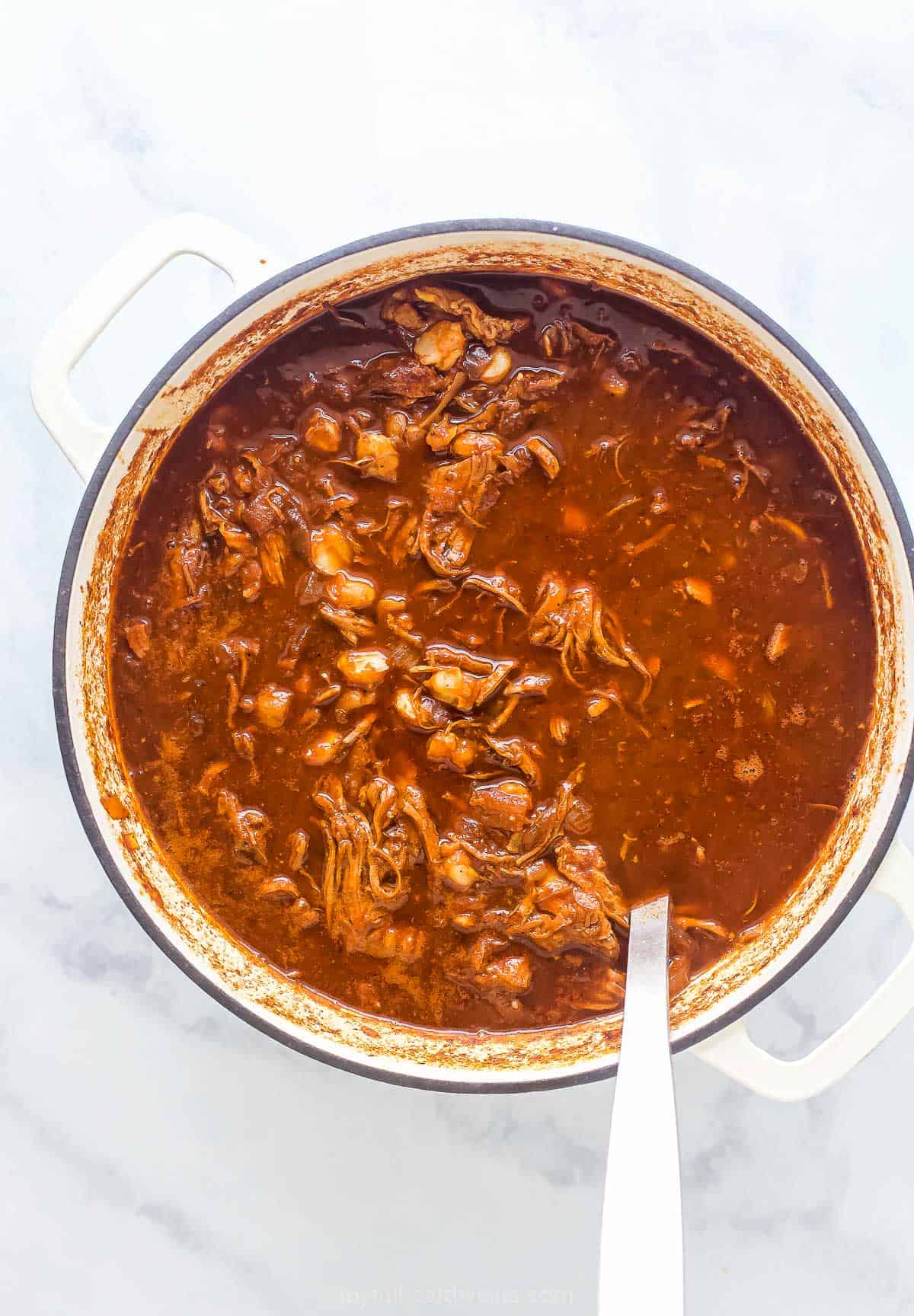 a pot of Mexican Chicken Stew with bits of pulled chicken and hominy in a brown broth