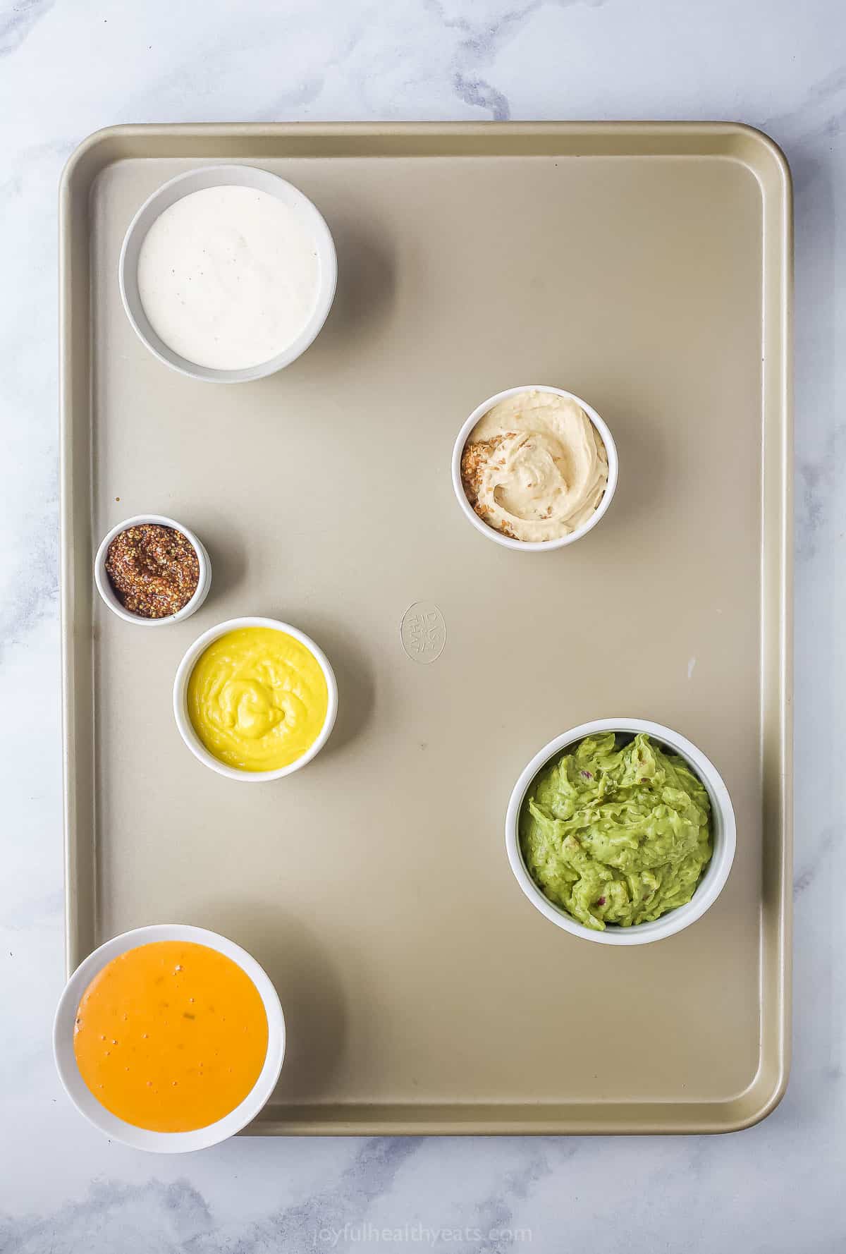 A baking tray with an assortment of appeitzer dips in small ramekins