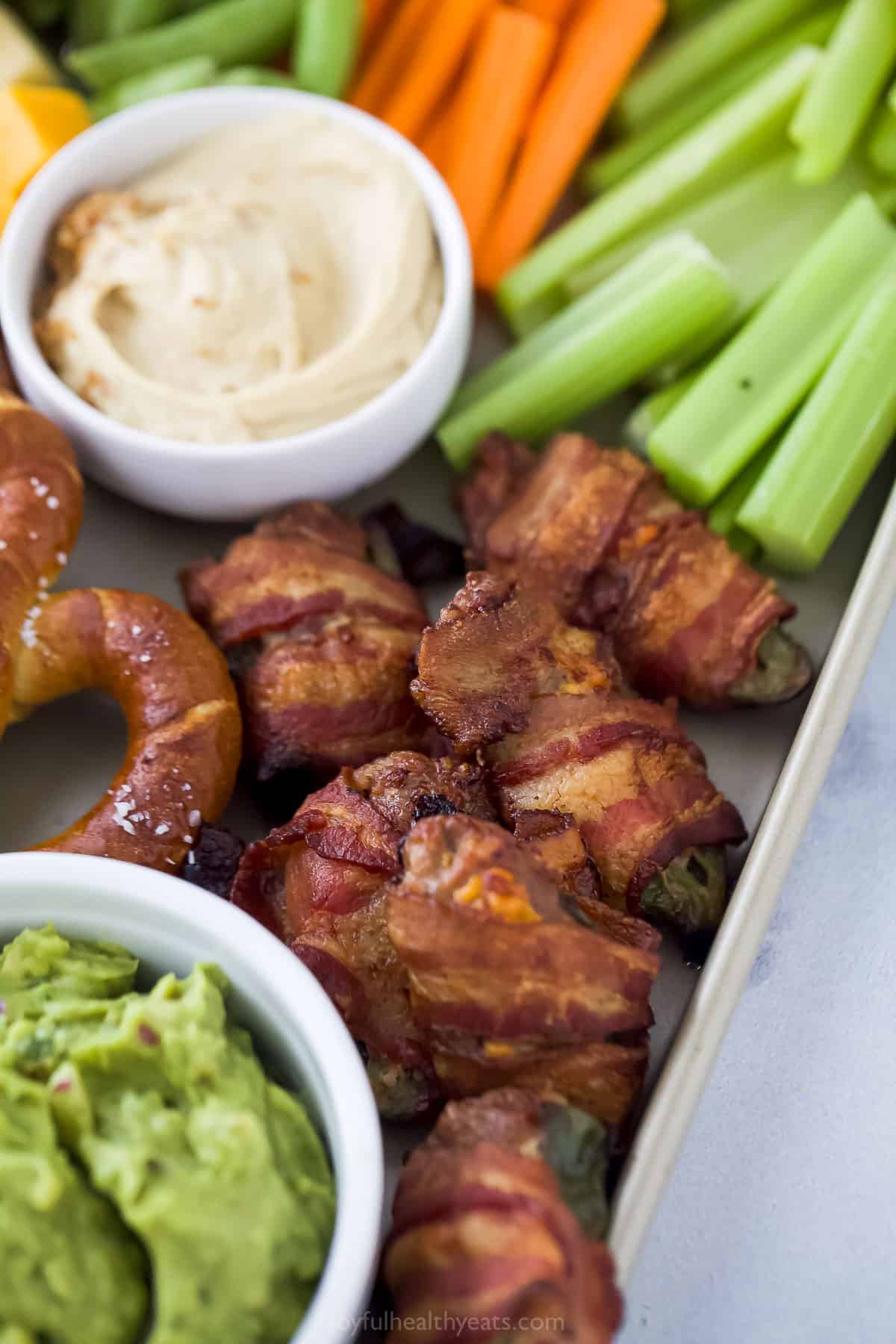 close up of bacon wrapped jalapenos on a tray with veggie sticks and dips