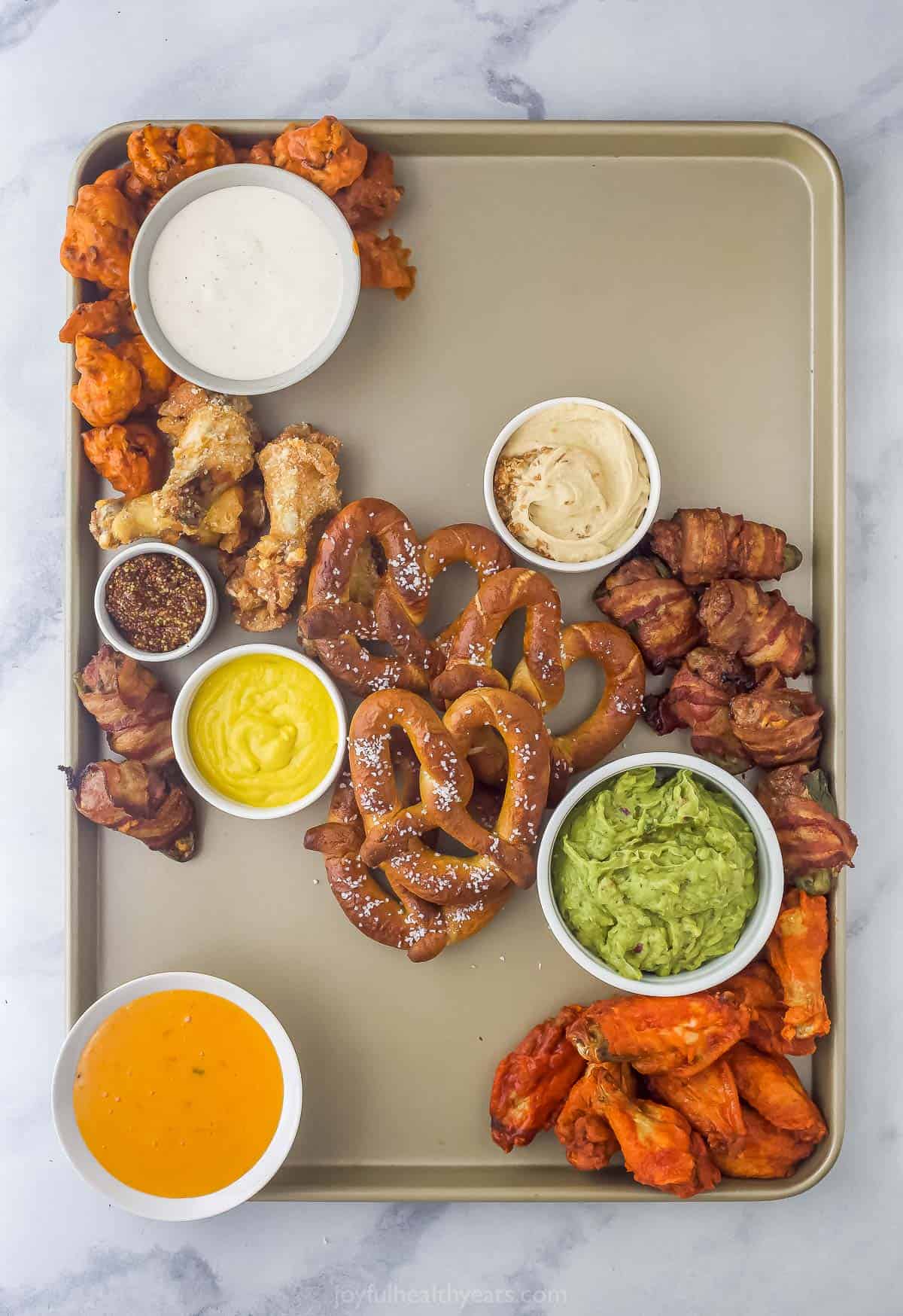 building a snacking board with an assortment of small bowls with dips, chicken wings, and pretzels
