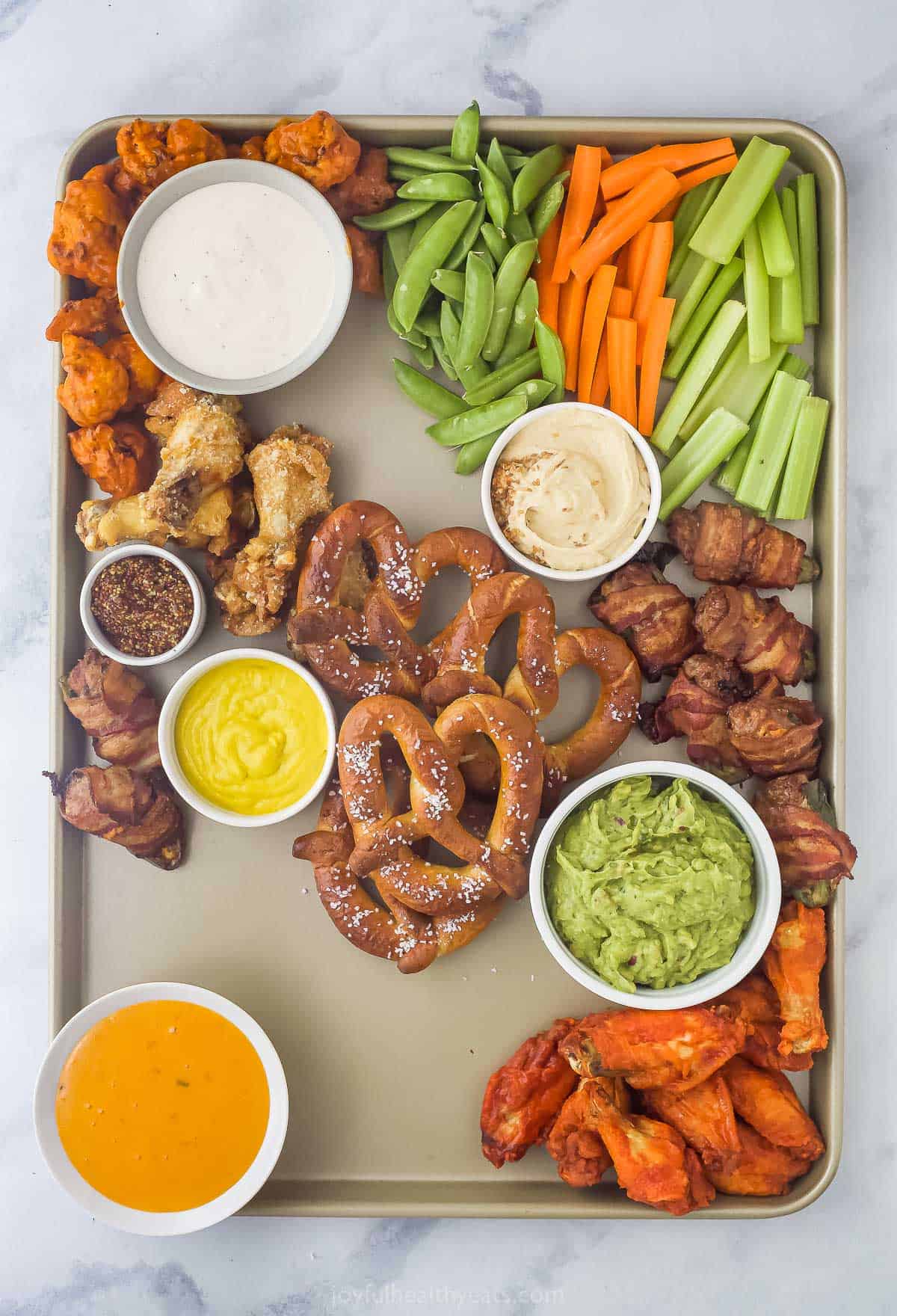 a snack platter with pretzels, chicken wings, cut up vegetables, and an assortment of dips
