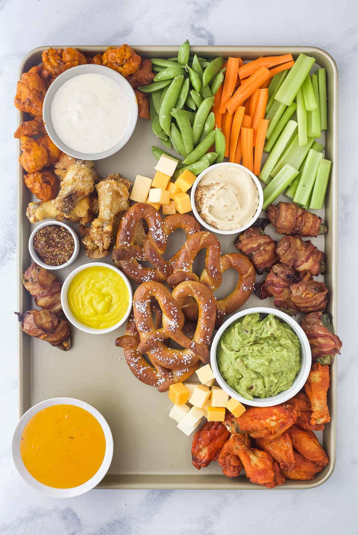 a snack platter with cheese cubes, pretzels, chicken wings, cut up vegetables, and an assortment of dips
