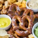 a close up of preztels on a food tray with an assortment of other dips and snacks