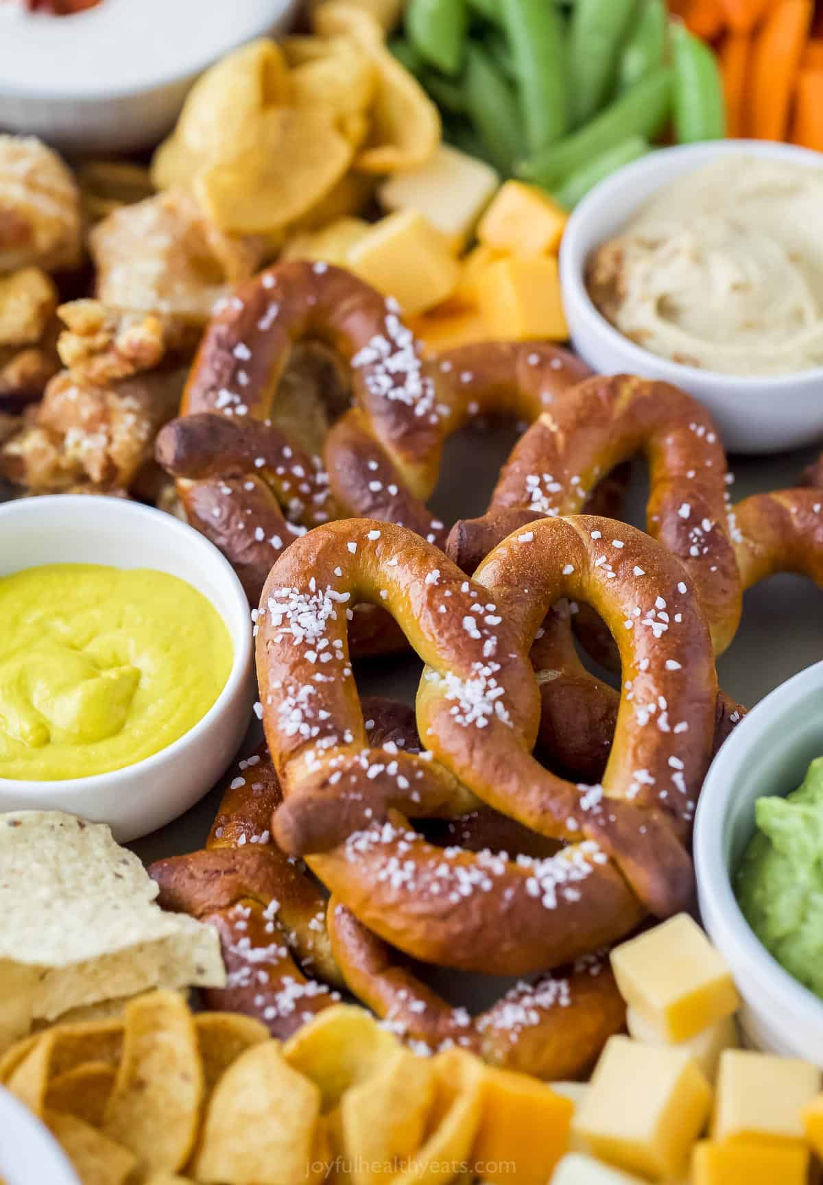 a close up of preztels on a food tray with an assortment of other dips and snacks