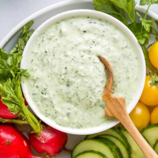 A bowl of green goddess dressing on a plate with fresh veggies