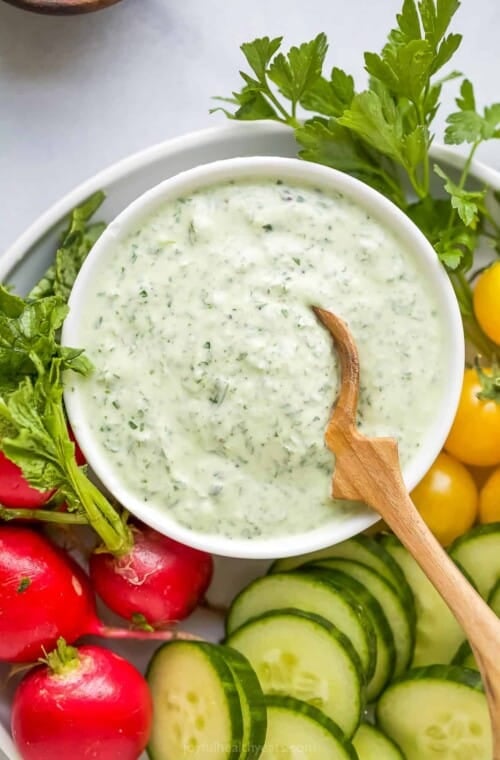 A bowl of green goddess dressing on a plate with fresh veggies