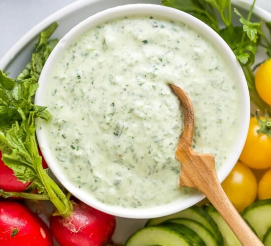 A bowl of green goddess dressing on a plate with fresh veggies