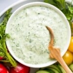 A bowl full of green goddess dressing with a small wooden spoon dipped inside