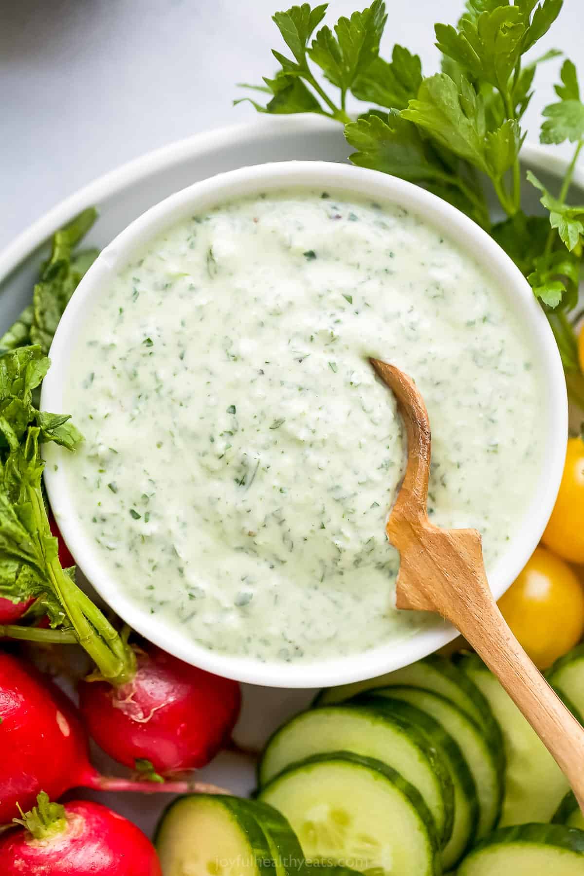 A bowl full of green goddess dressing with a small wooden spoon dipped inside