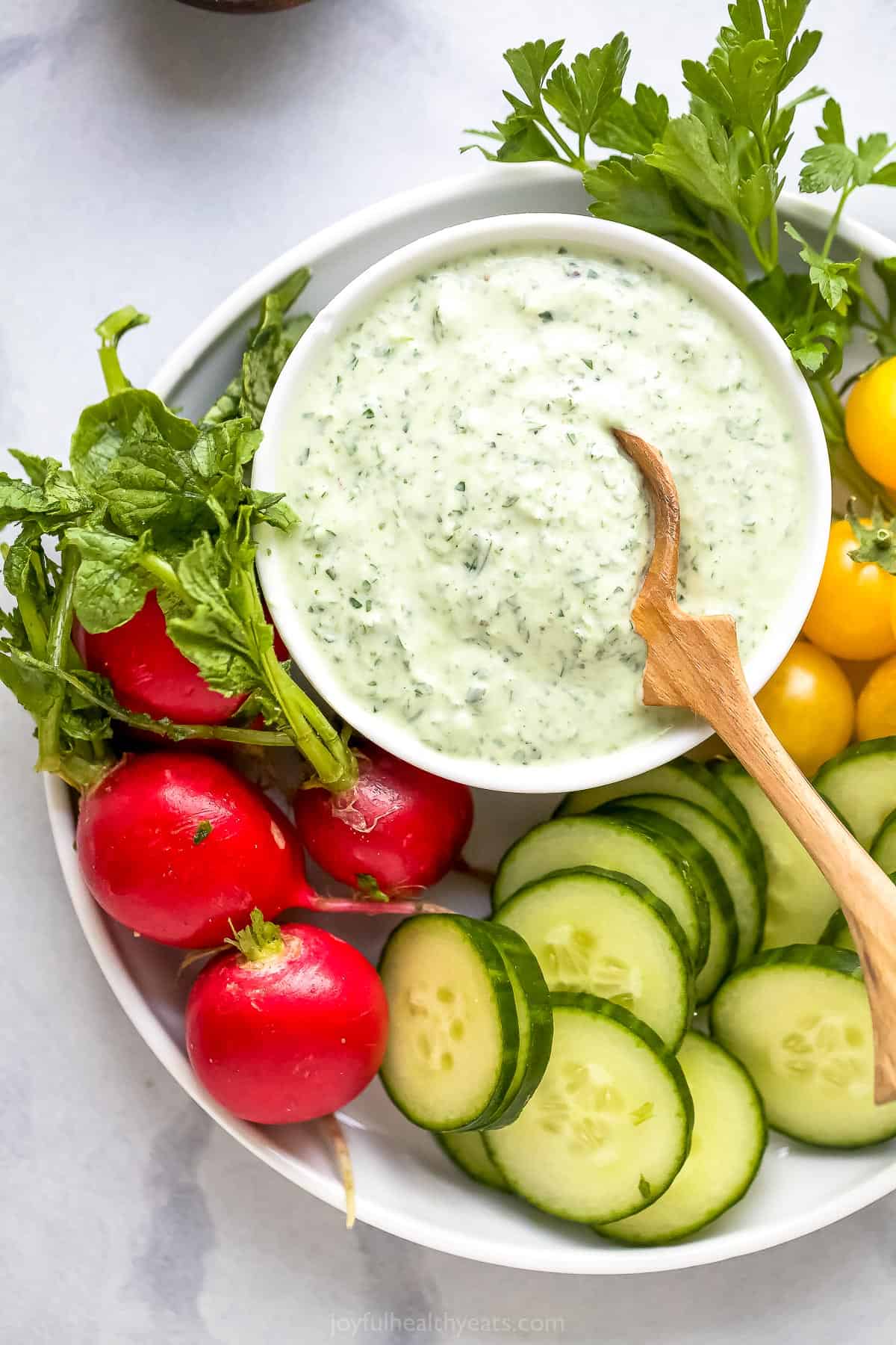 A plate of raw veggies with a dish of green goddess dressing beside them