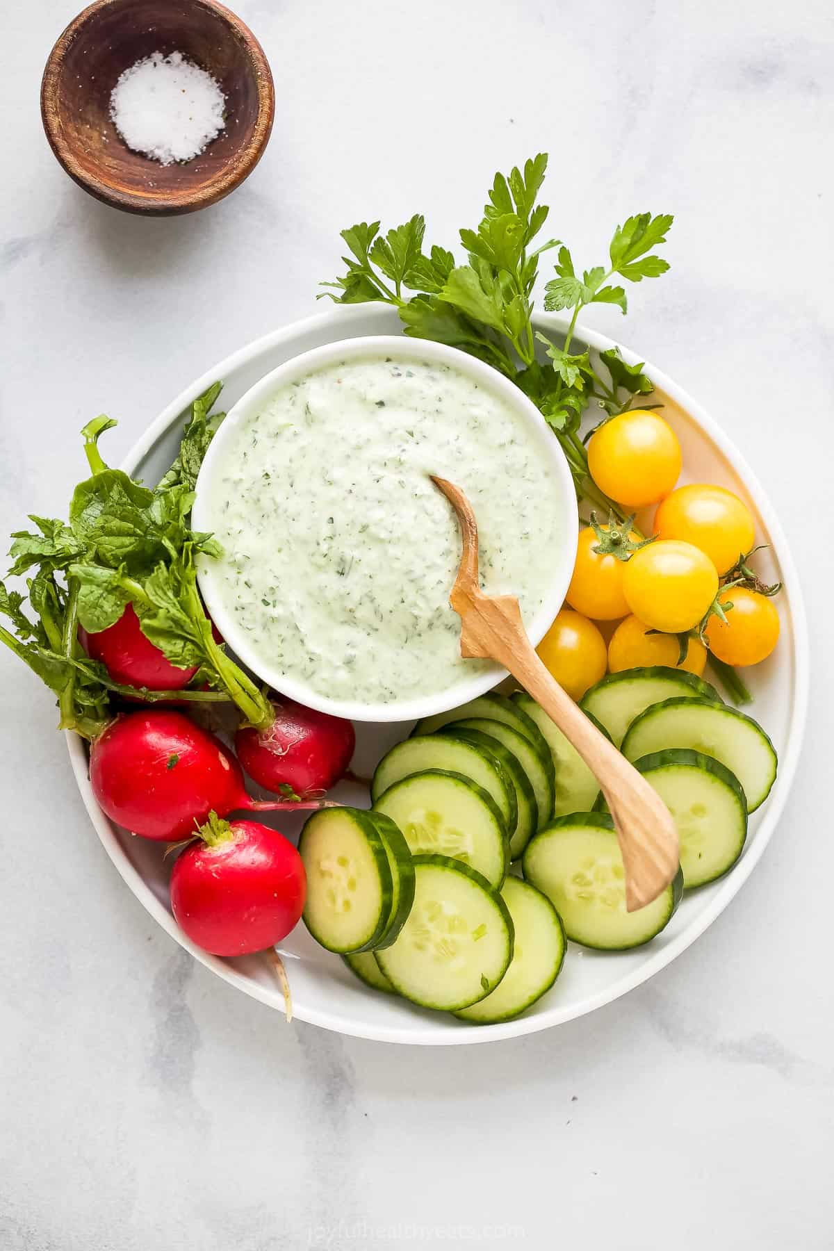 Crudités on a plate with green goddess dip and a small dish of salt beside the plate