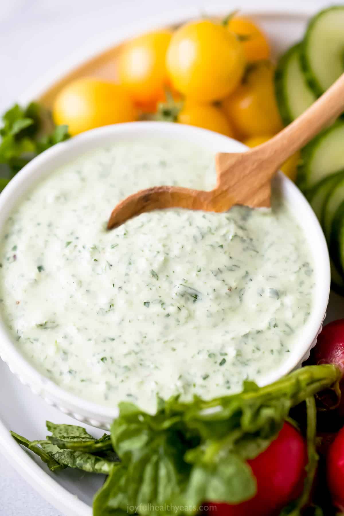 A close-up shot of a wooden spoon digging into a dish full of green goddess dressing