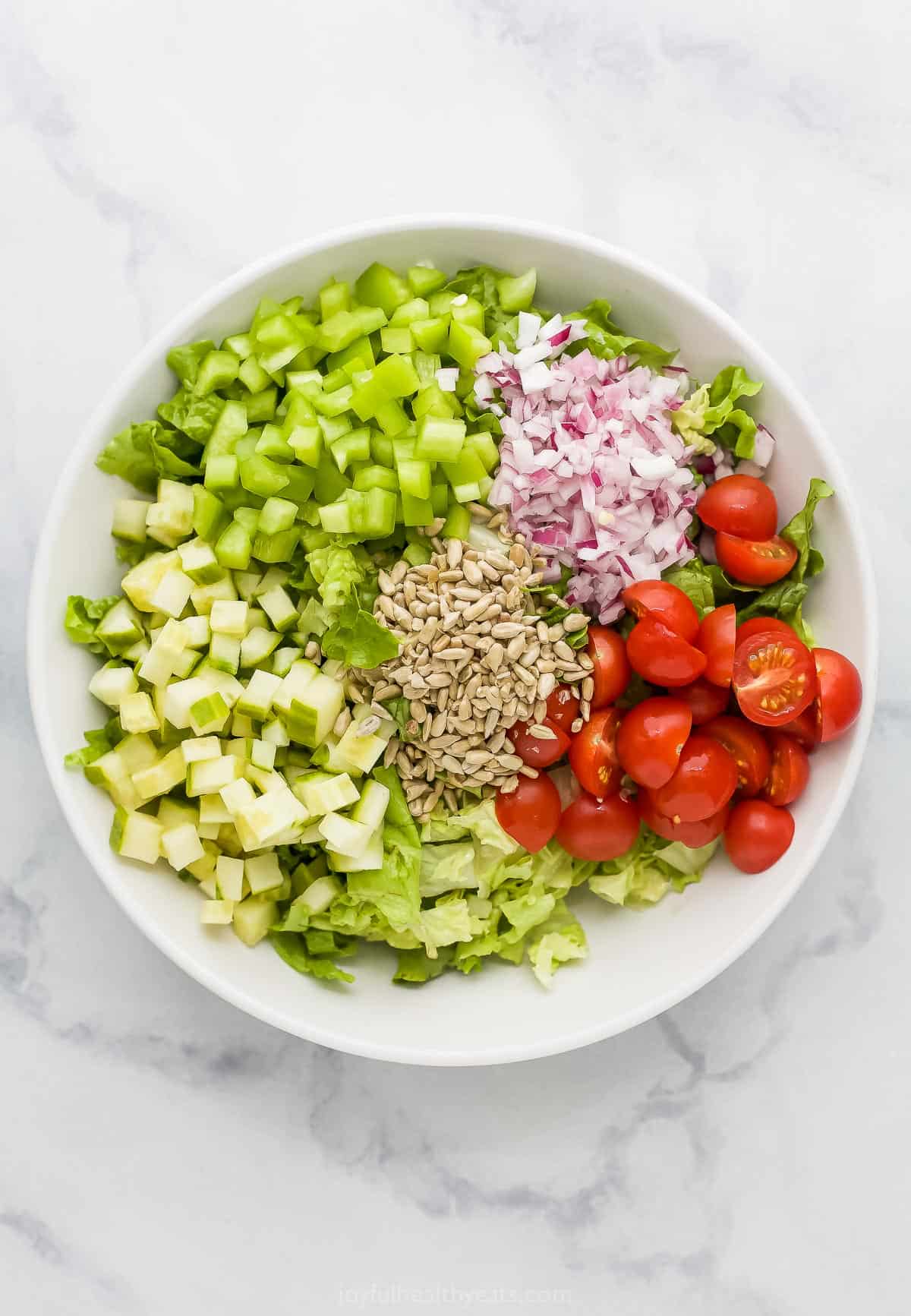 All of the prepared salad ingredients in a bowl on a marble kitchen countertop