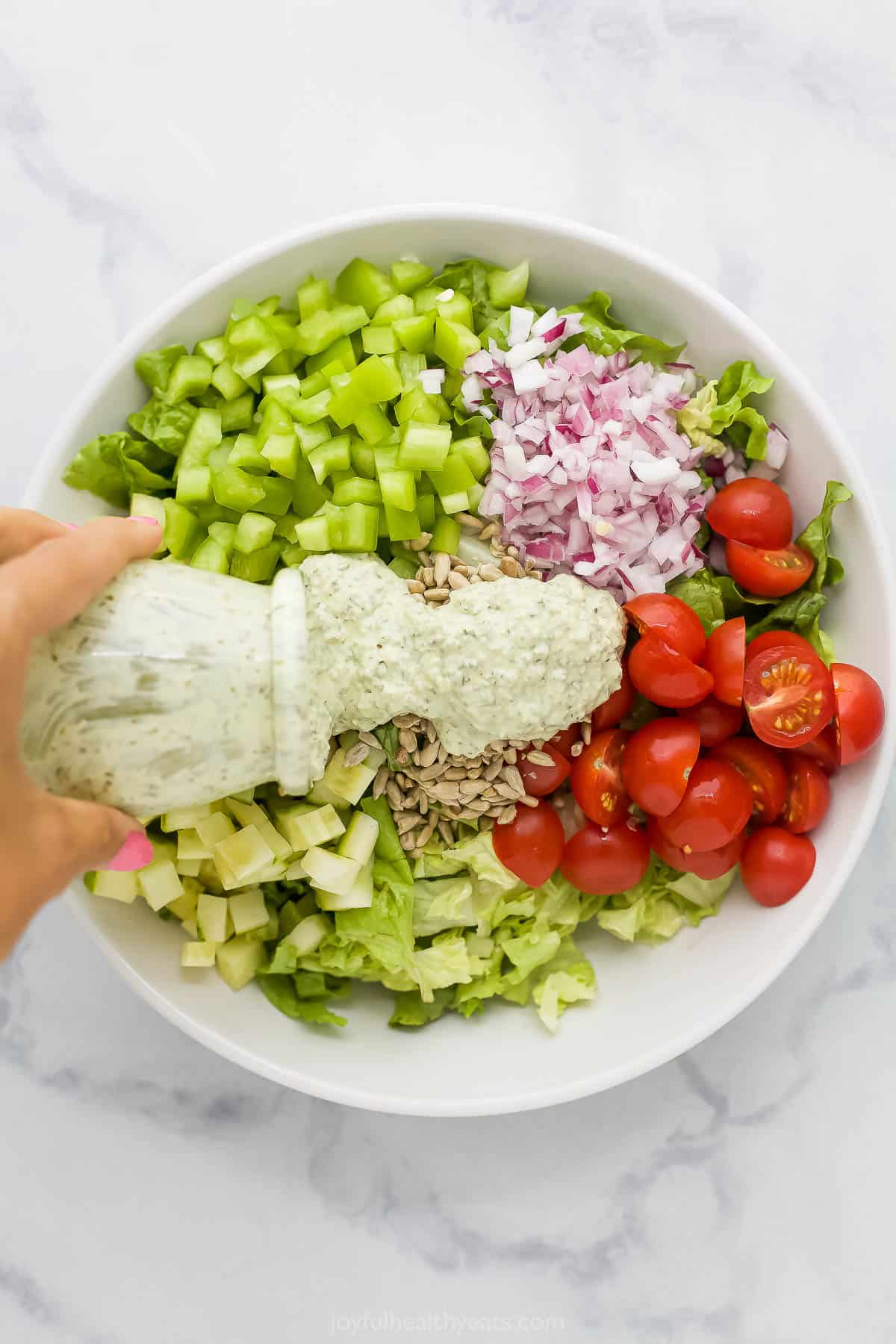 Green goddess dressing being poured from a jar into a bowl full of veggies and sunflower seeds