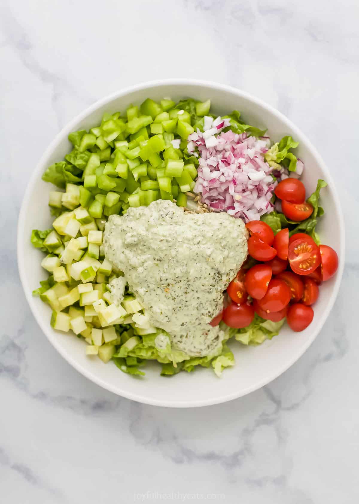 A big bowl of salad sitting on a white and gray marble surface